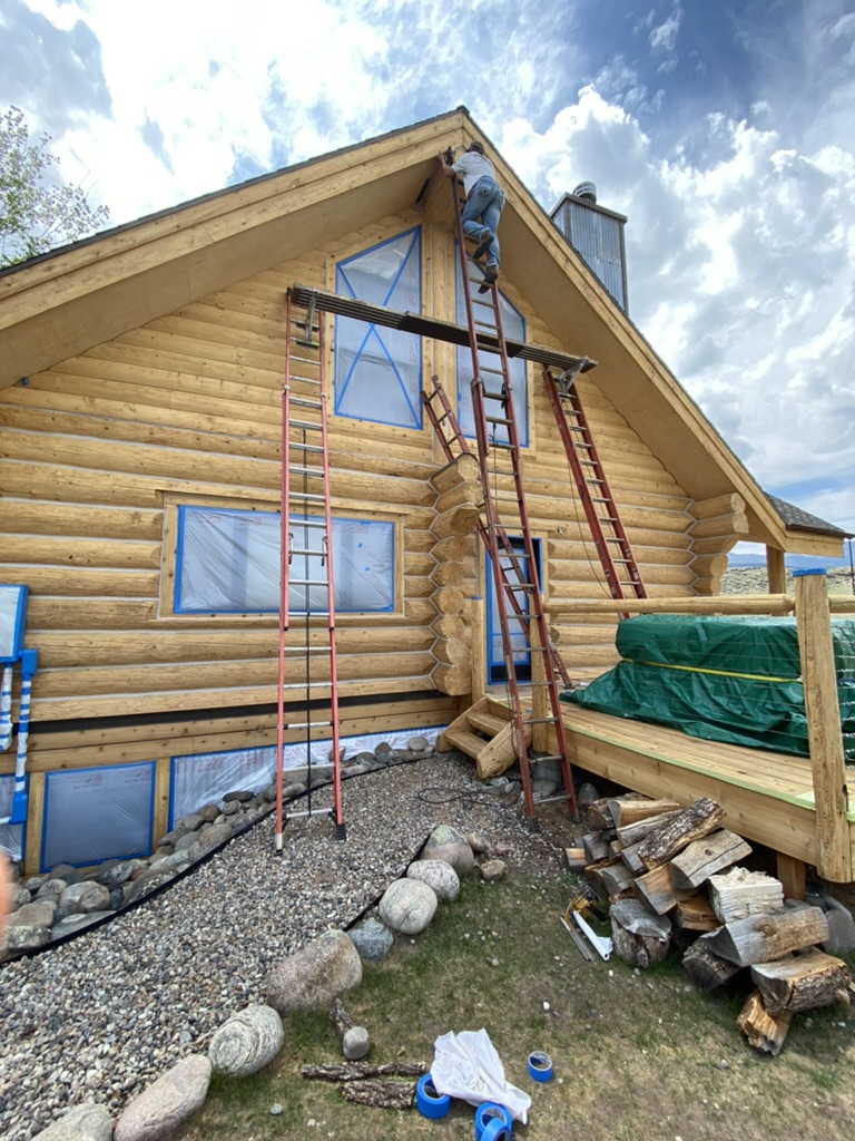 Log home restoration in progress with ladders and masking